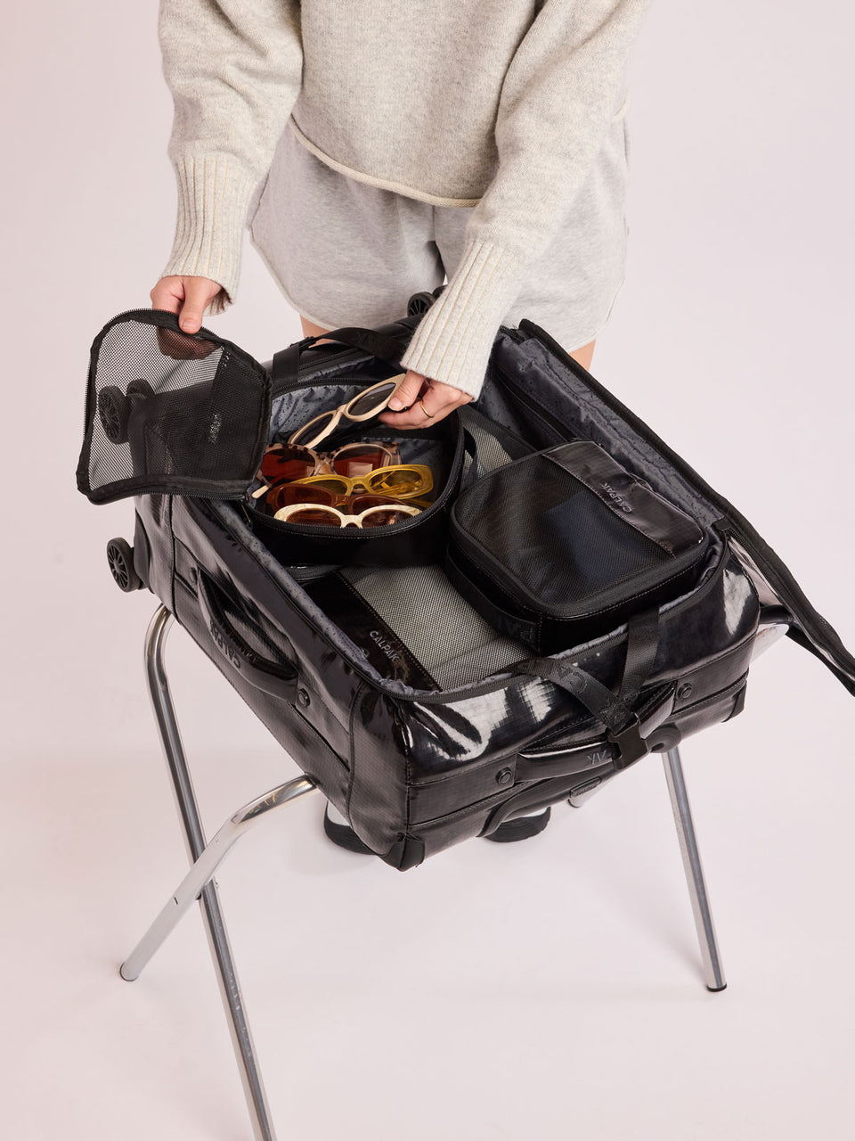 Model packing luggage and adding sunglasses into the CALPAK Terra 5-Piece Packing Cube Set in black Obsidian with two small cubes, two medium cubes, and one large mesh cube with zippers and mesh; PCT2601-OBSIDIAN