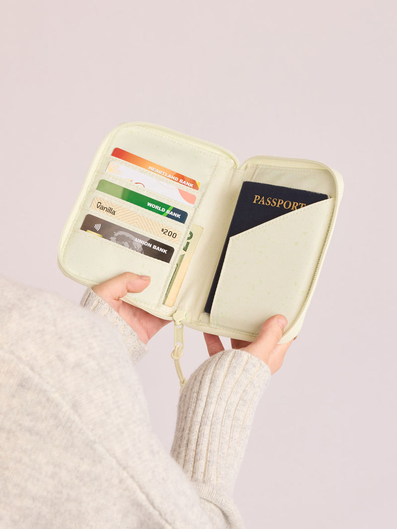 Person holding open Front side of CALPAK Terra Zip Passport Wallet in light green Celadon
