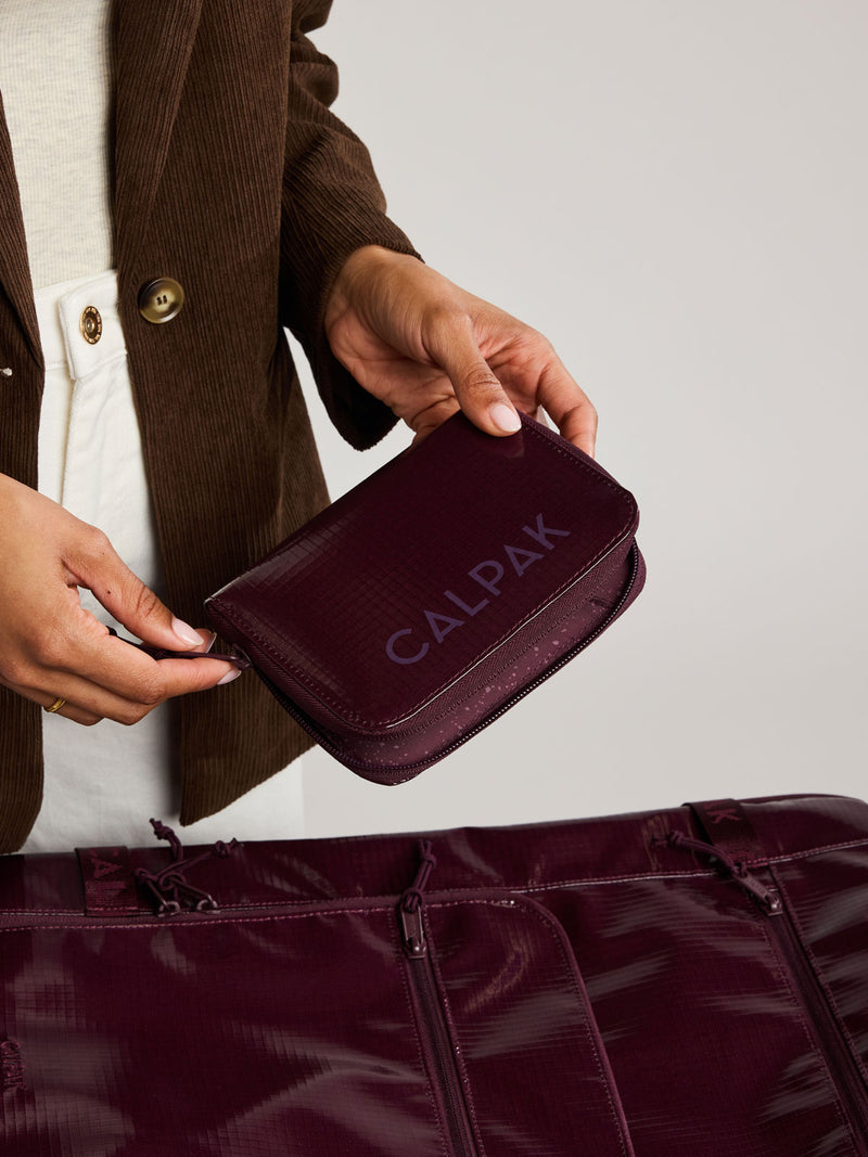Person holding the  CALPAK Terra Zip Passport Wallet in dark red Dark Cherry on a white background