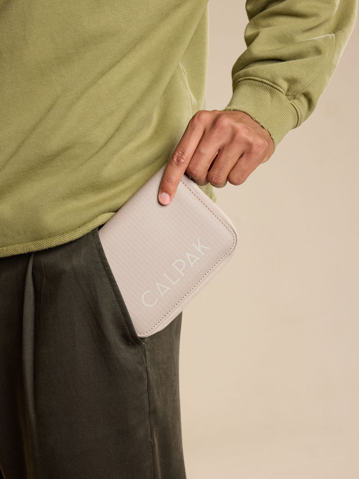 Model with CALPAK Terra Zippered Passport Wallet in beige Stone front view; ATPW2501-STONE