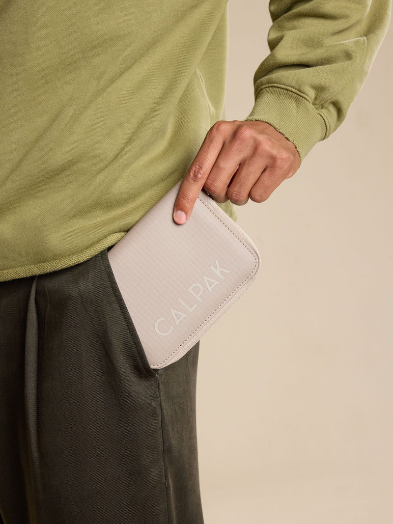Model with CALPAK Terra Zippered Passport Wallet in beige Stone front view