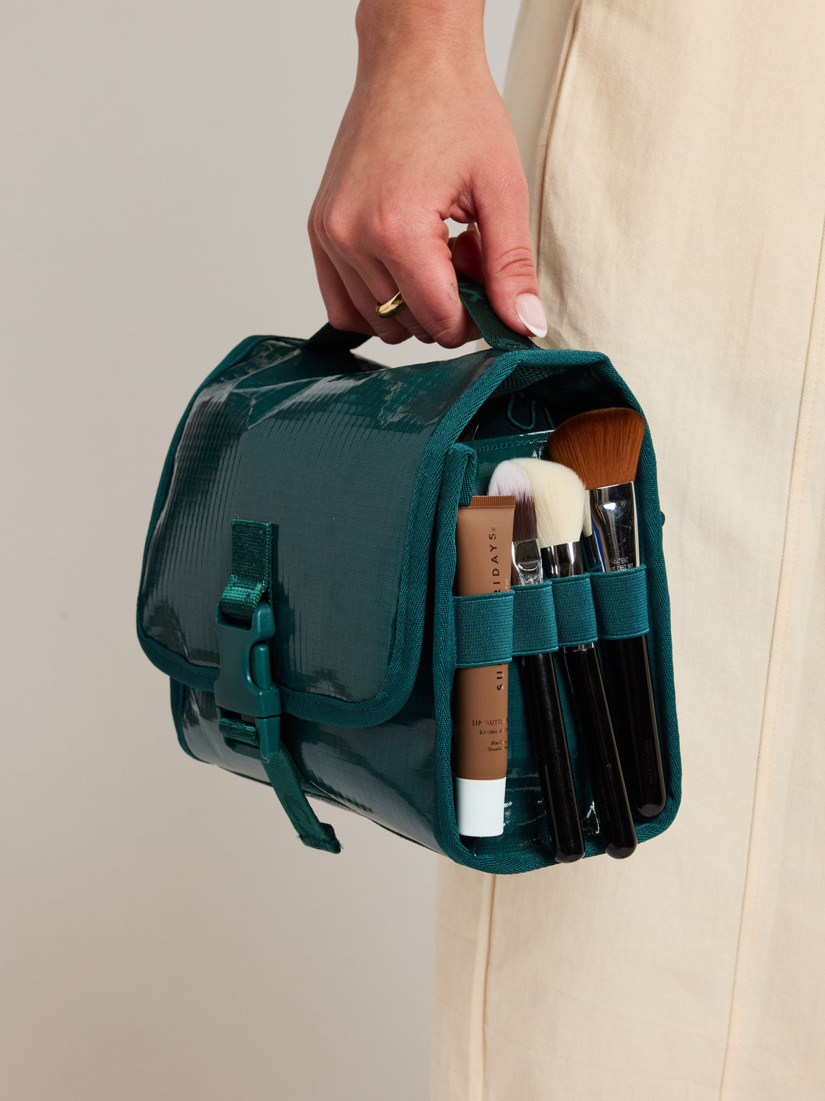 Person carrying the CALPAK Terra Hanging Toiletry Bag to store makeup and toiletries in blue green Kale on a white background; THY2201-KALE