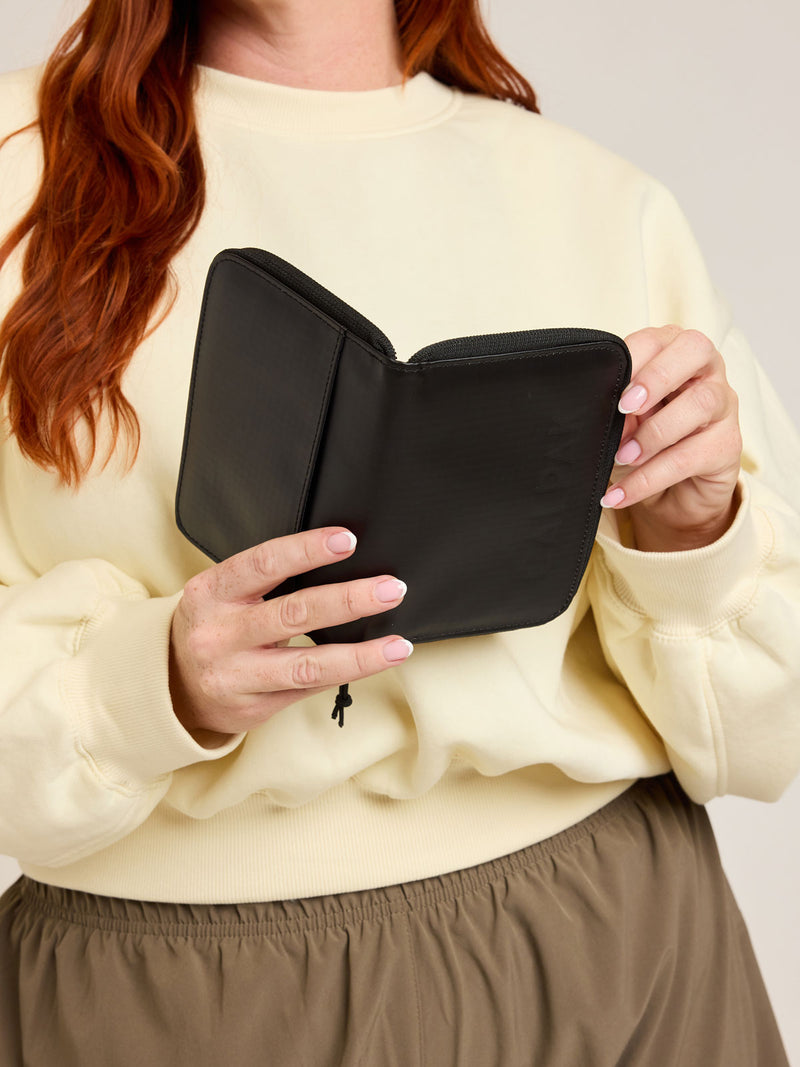 Model with CALPAK Terra Zippered Passport Wallet in black Matte Obsidian front view