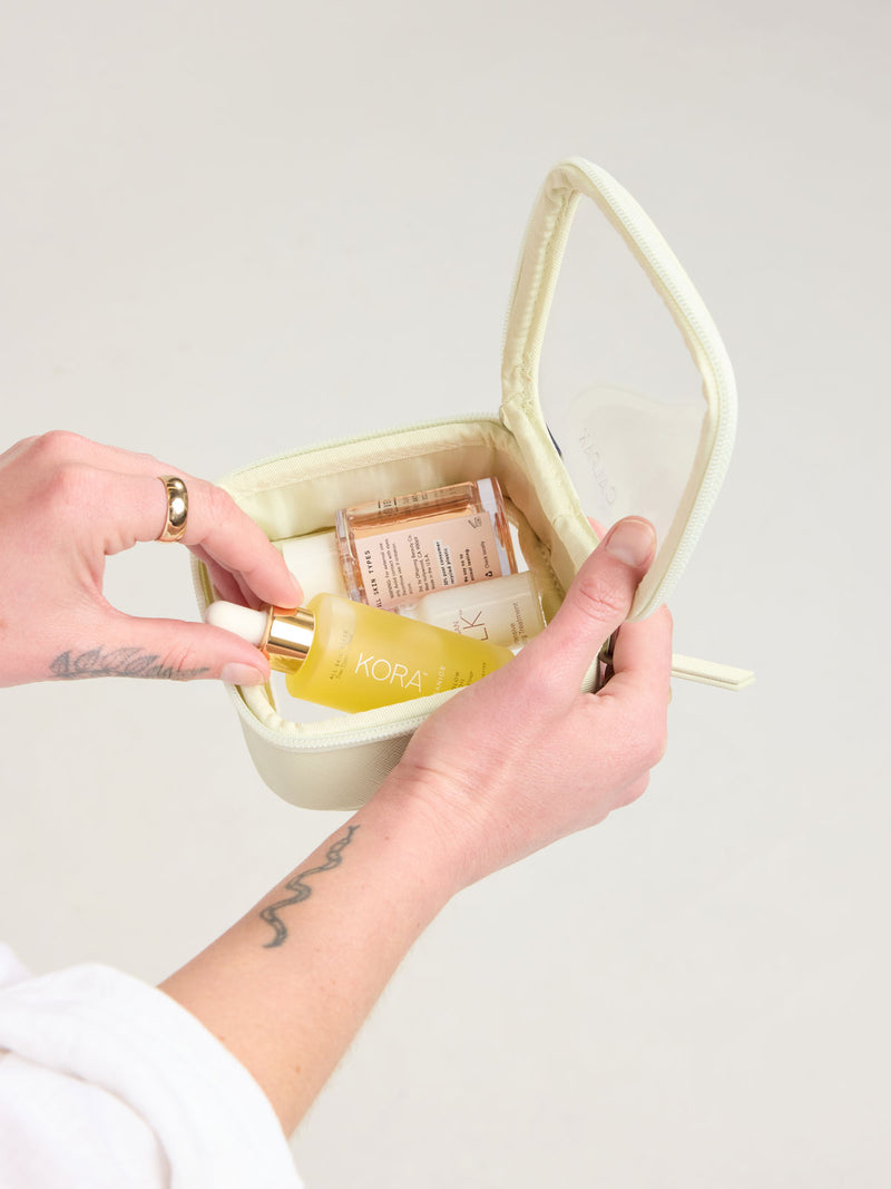 Person adding toiletry into CALPAK Tiny Clear Cosmetic Case in light green Celadon