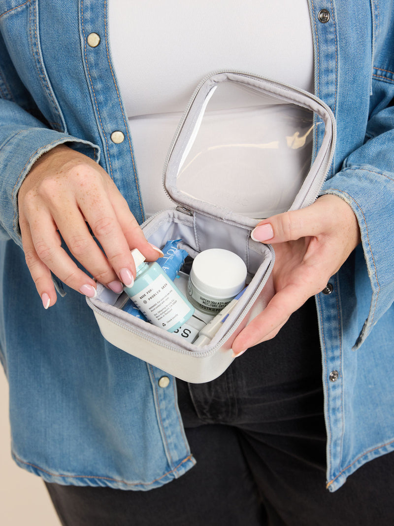Model adding items into the CALPAK Tiny Clear Cosmetics Case in Silver