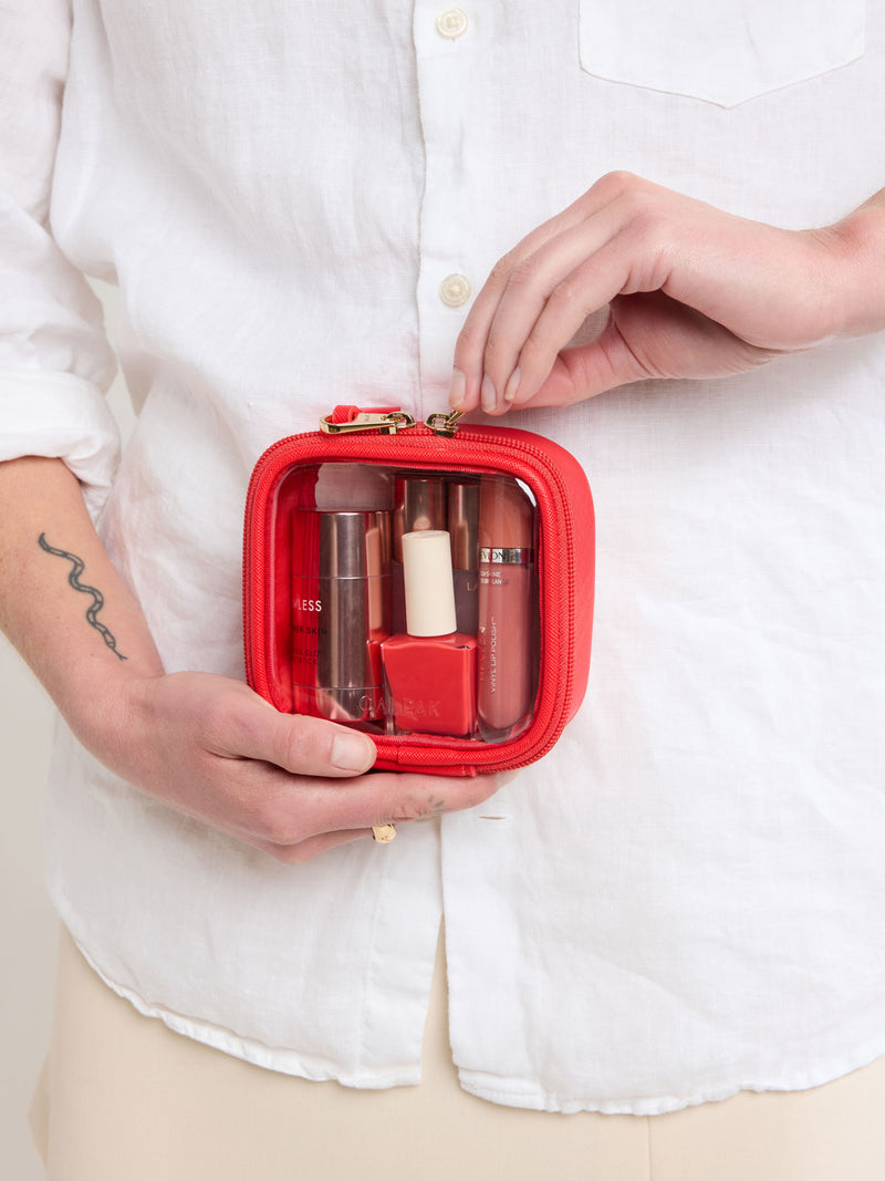 Person closing zipper of CALPAK Tiny Clear Cosmetic Case in red Tomato