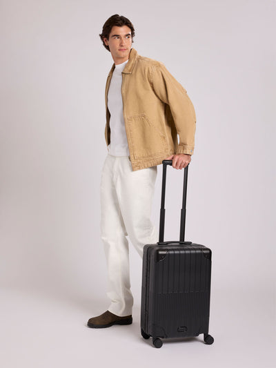 CALPAK Vault black Onyx hard-shell spinner Carry On Luggage with a telescoping handle extended, featuring a Black leatherette side handle and trim, set against a plain light gray background; LVT1020-ONYX view 2
