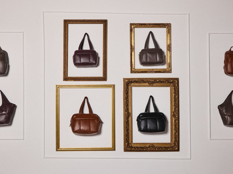 A wall-mounted art piece featuring four framed vegan leather CALPAK Luka Collection handbag illustrations or photographs in different colors and ornate gold frames, arranged on a white mat against a light wall.