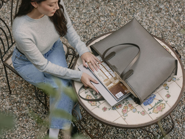 Woman pulling out a magazine and laptop from CALPAK Colette Laptop Tote on a round table outdoors