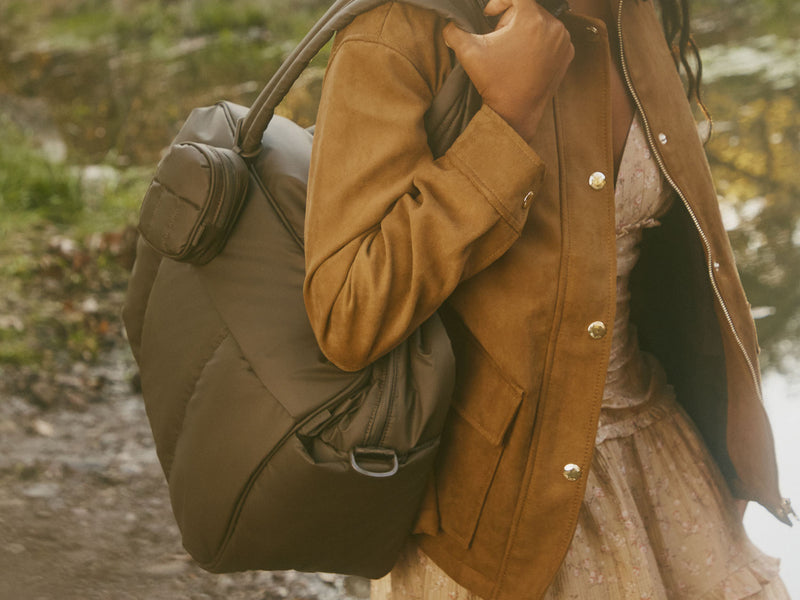 Person wearing a brown jacket holding a large brown CALPAK Luka Duffel outdoors.