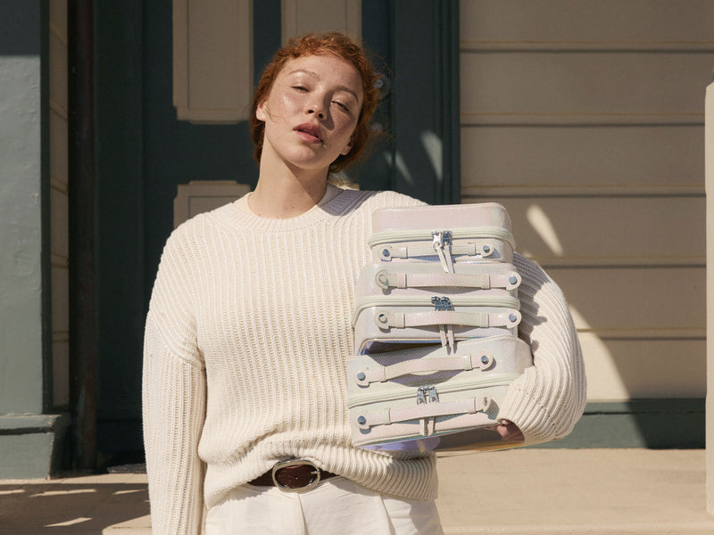 Woman holding a stack of iridescent Moonbeam Clear Cosmetics Cases outside a building