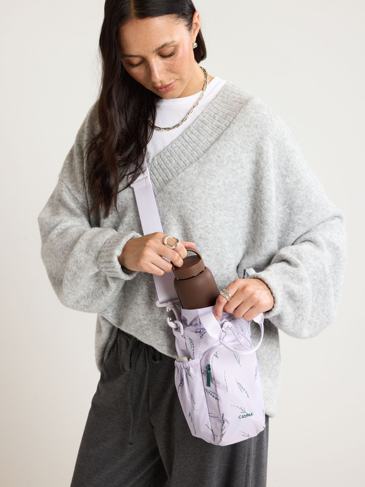 Person with CALPAK Water Bottle Holder in lavender purple with lavender flower print ; AWH2101-LAVENDER-BLOOM