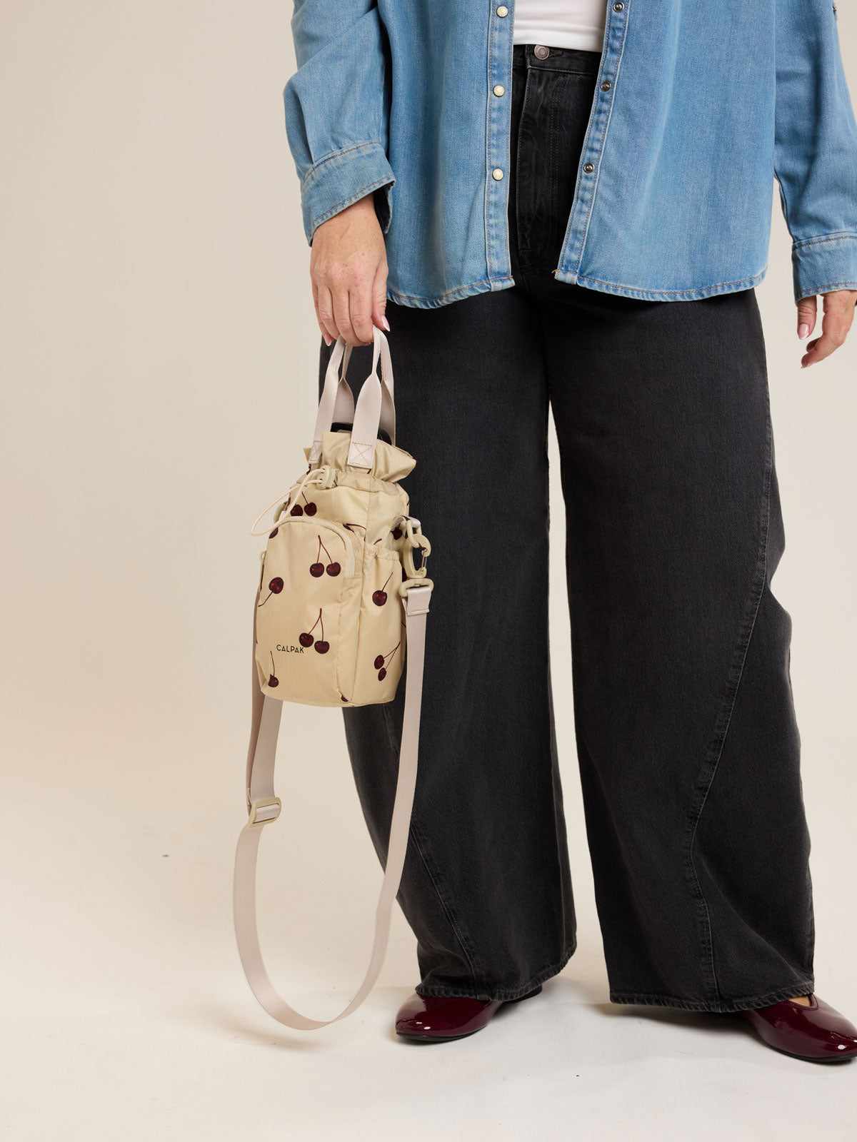 Model holding CALPAK Water Bottle Holder in Oatmeal Chery in beige with cherry pattern; AWH2101-OATMEAL-CHERRY