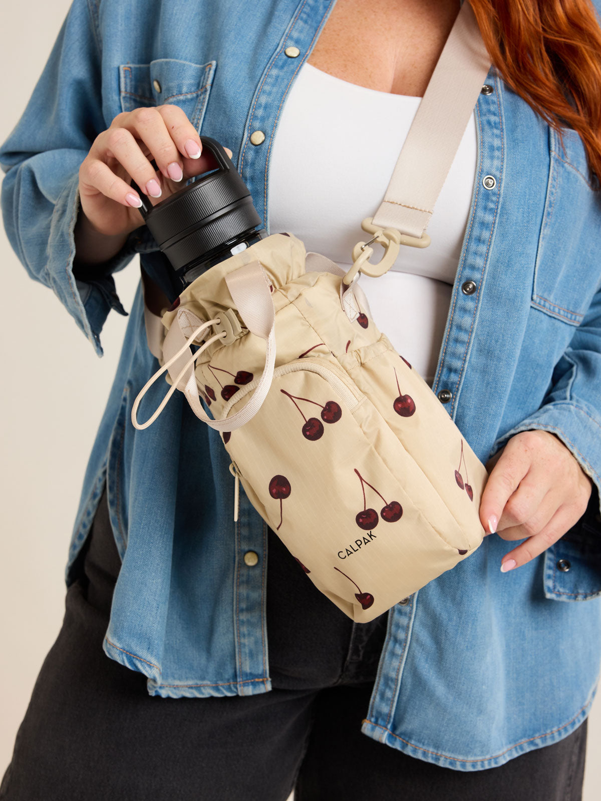 Model with CALPAK Water Bottle Holder in Oatmeal Chery in beige with cherry pattern; AWH2101-OATMEAL-CHERRY