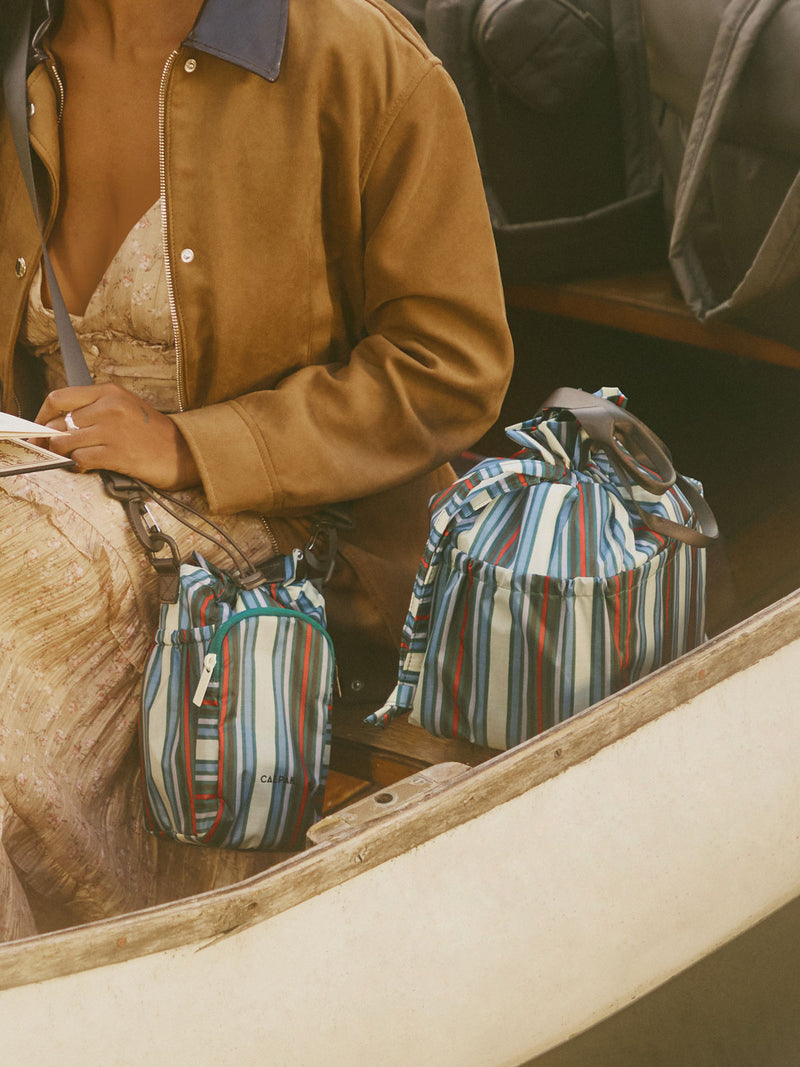 Person wearing CALPAK Water Bottle Holder in multicolor stripe Riviera Stripe