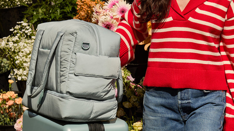 Bluebell CALPAK Weekend Duffel on a luggage with a person wearing a red and white striped sweater in the background.