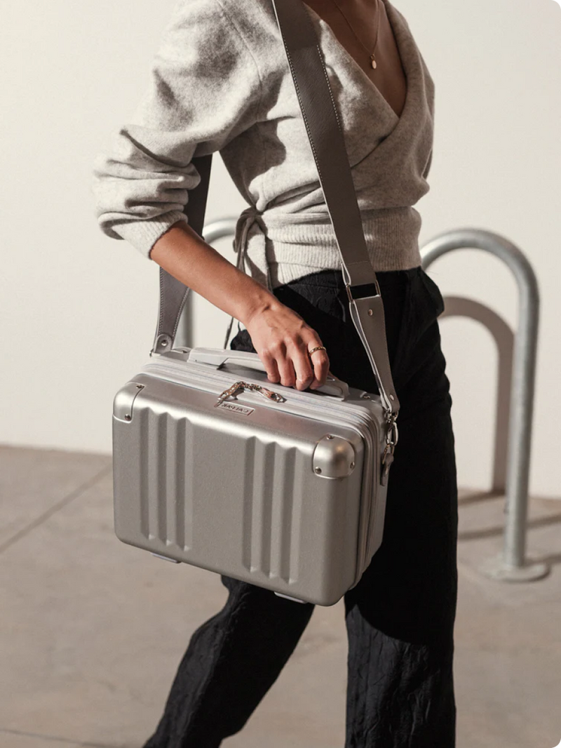 Model using crossbody strap to carry CALPAK Ambeur Vanity Case in silver