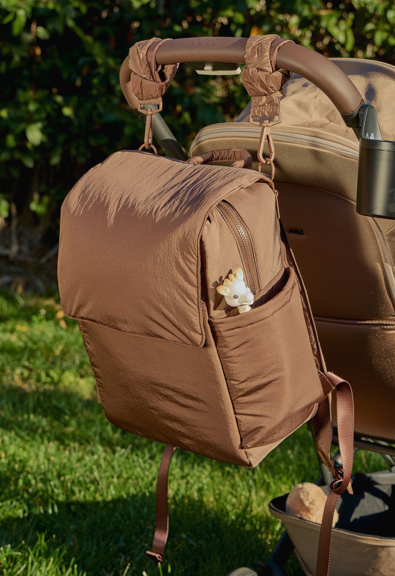 CALPAK Diaper Backpack in brown Hazelnut hanging on a stroller with CALPAK brown Hazelnut Stroller Straps