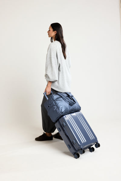 Person in a grey sweater with CALPAK Carry On Luggage in blue Indigo with the Luka Duffel in blue Indigo