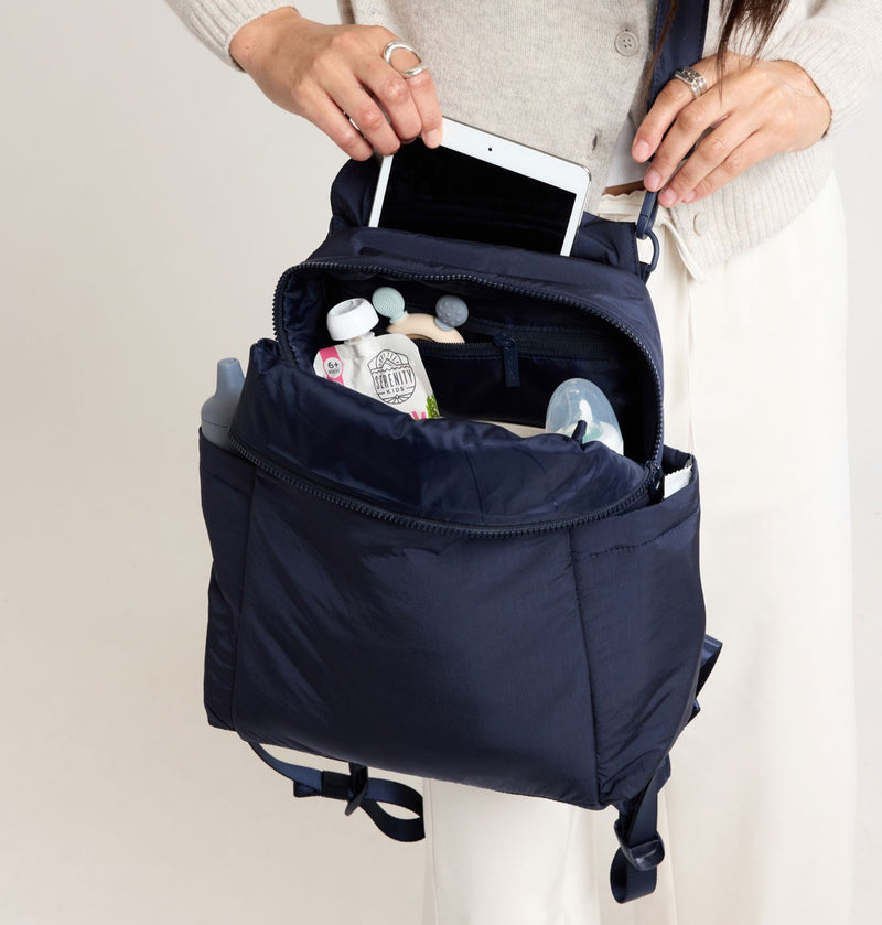 CALPAK Mini Diaper Bag in Navy blue backpack with items inside on a neutral background