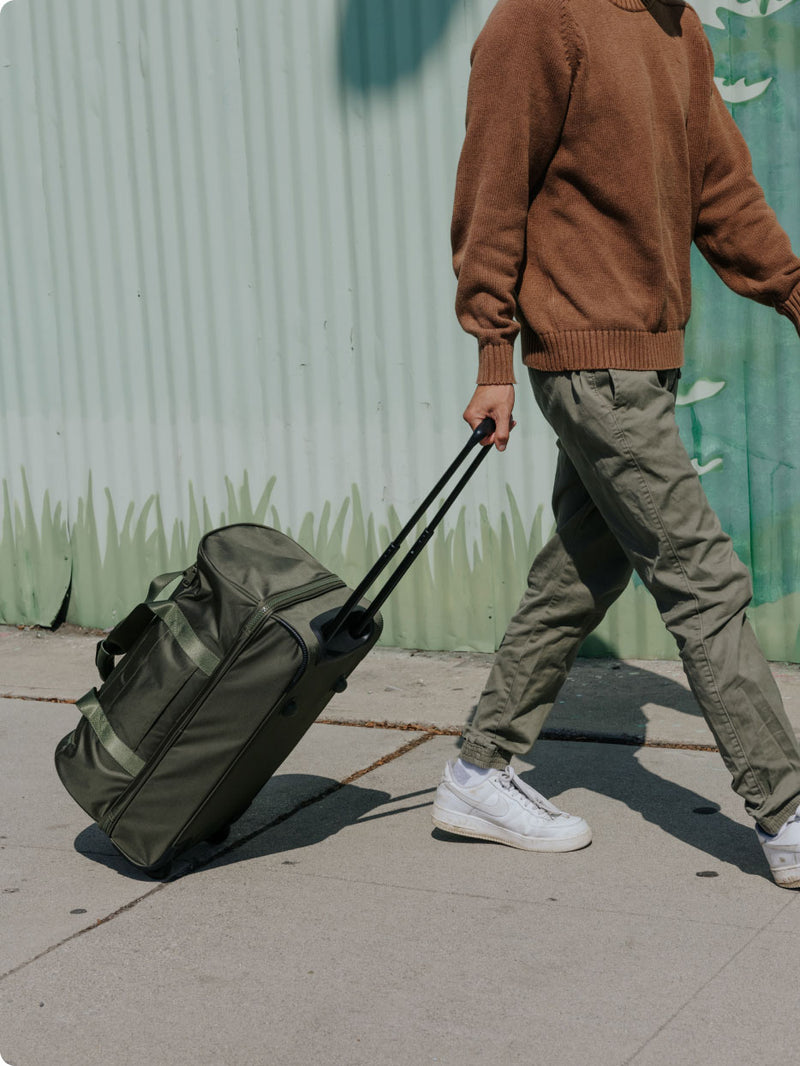 Model rolling the Stevyn Rolling Duffel Bag in Green down a street