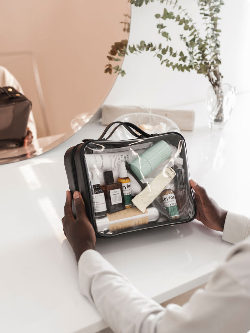Model holding black CALPAK Large Cosmetics Case filled with skin care and cosmetics