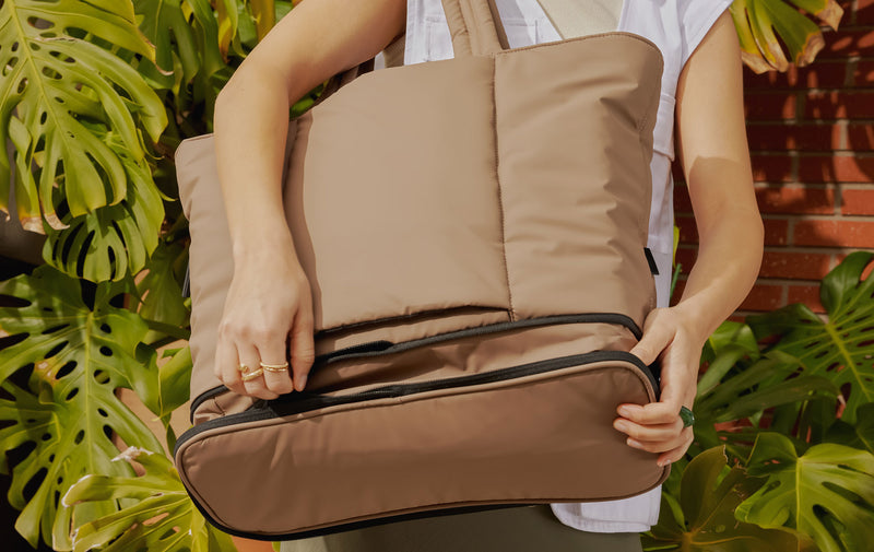 Model zipping up the expandable feature of the CALPAK Luka Expandable Tote in brown Chocolate