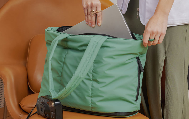 CALPAK Luka Expandable Tote in green with model putting in laptop