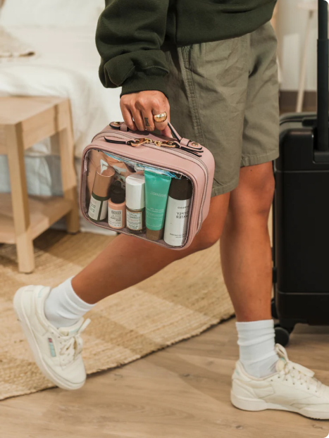 Model holding CALPAK Medium Clear Cosmetics Case filled with skincare products