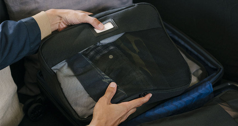 CALPAK 5 piece Packing Cube set in black being packed into a suitcases by model