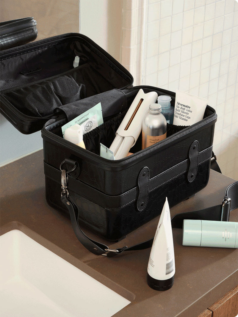 Black CALPAK Trnk Vanity Case on bathroom counter. Case is open and filled with toiletries, cosmetics and skincare products