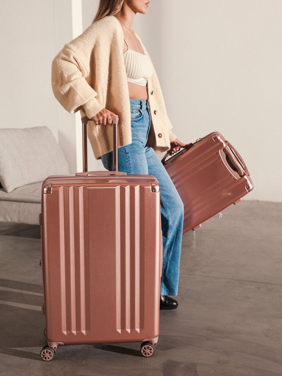 female model rolling 2 piece CALPAK Ambeur rose gold suitcases set