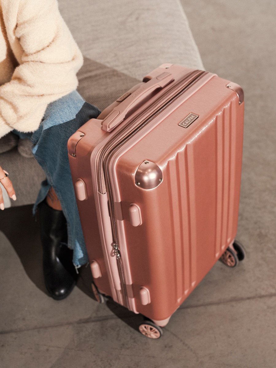 woman with rose gold CALPAK Ambeur hard shell rolling carry on