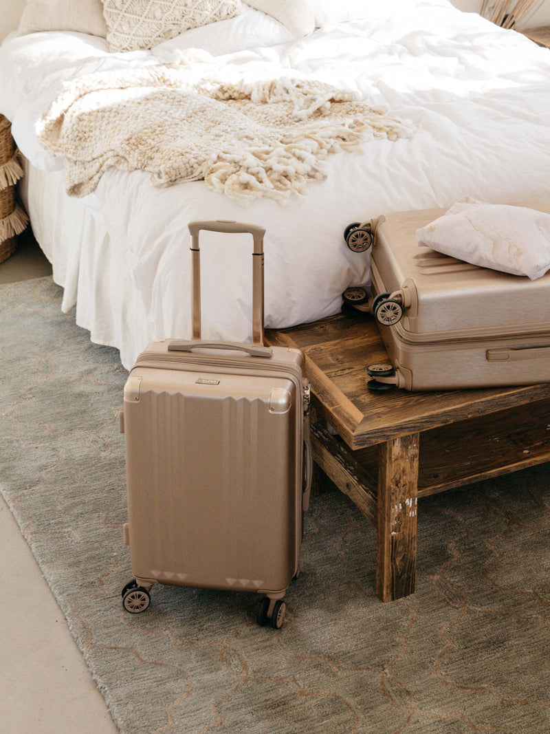 CALPAK Ambeur Carry-On Luggage in gold in bedroom
