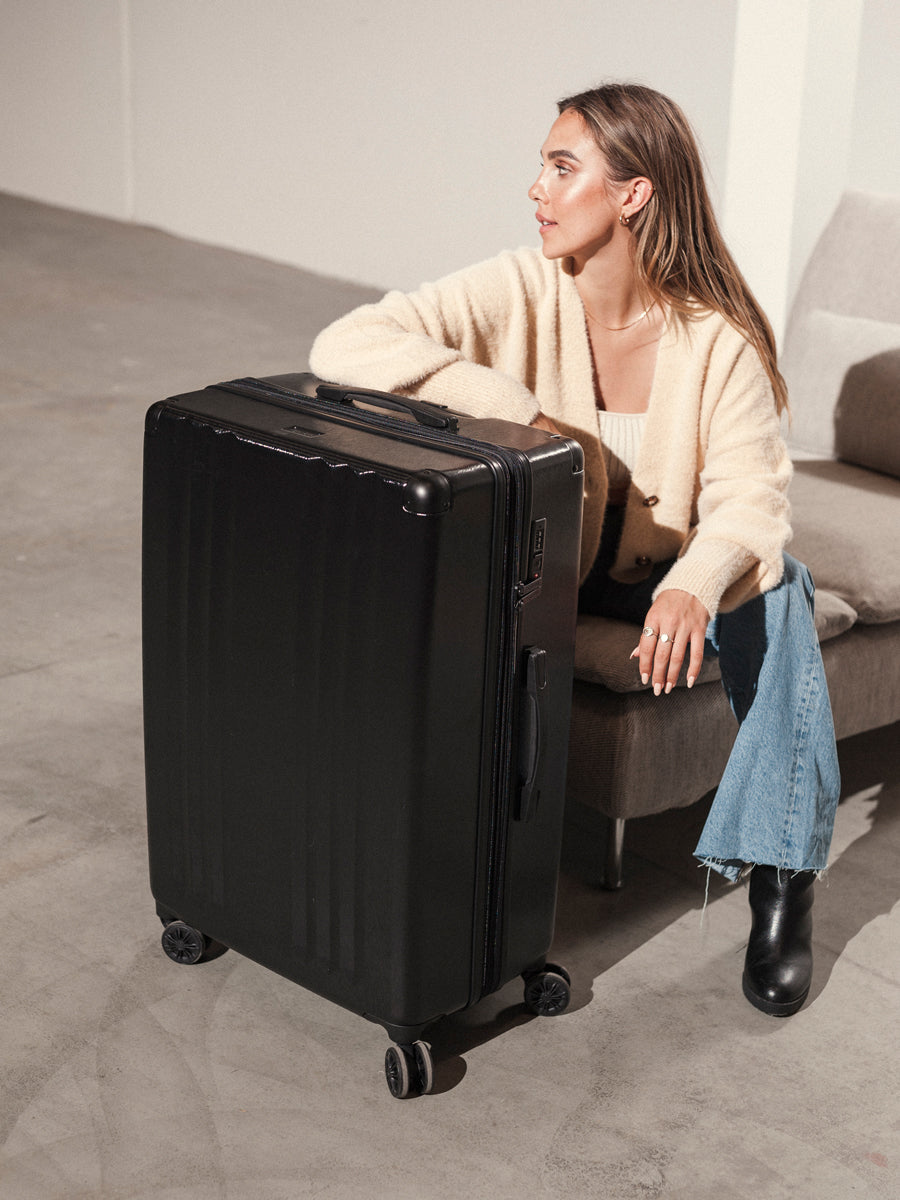 woman with large black CALPAK Ambeur hard shell spinner luggage