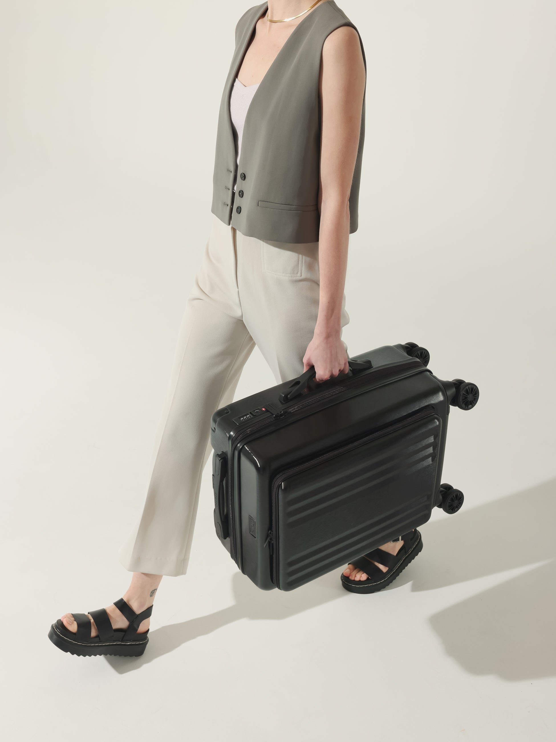 Model carrying CALPAK Ambeur hard shell carry-on with front pocket, cushioned top and side handles in black