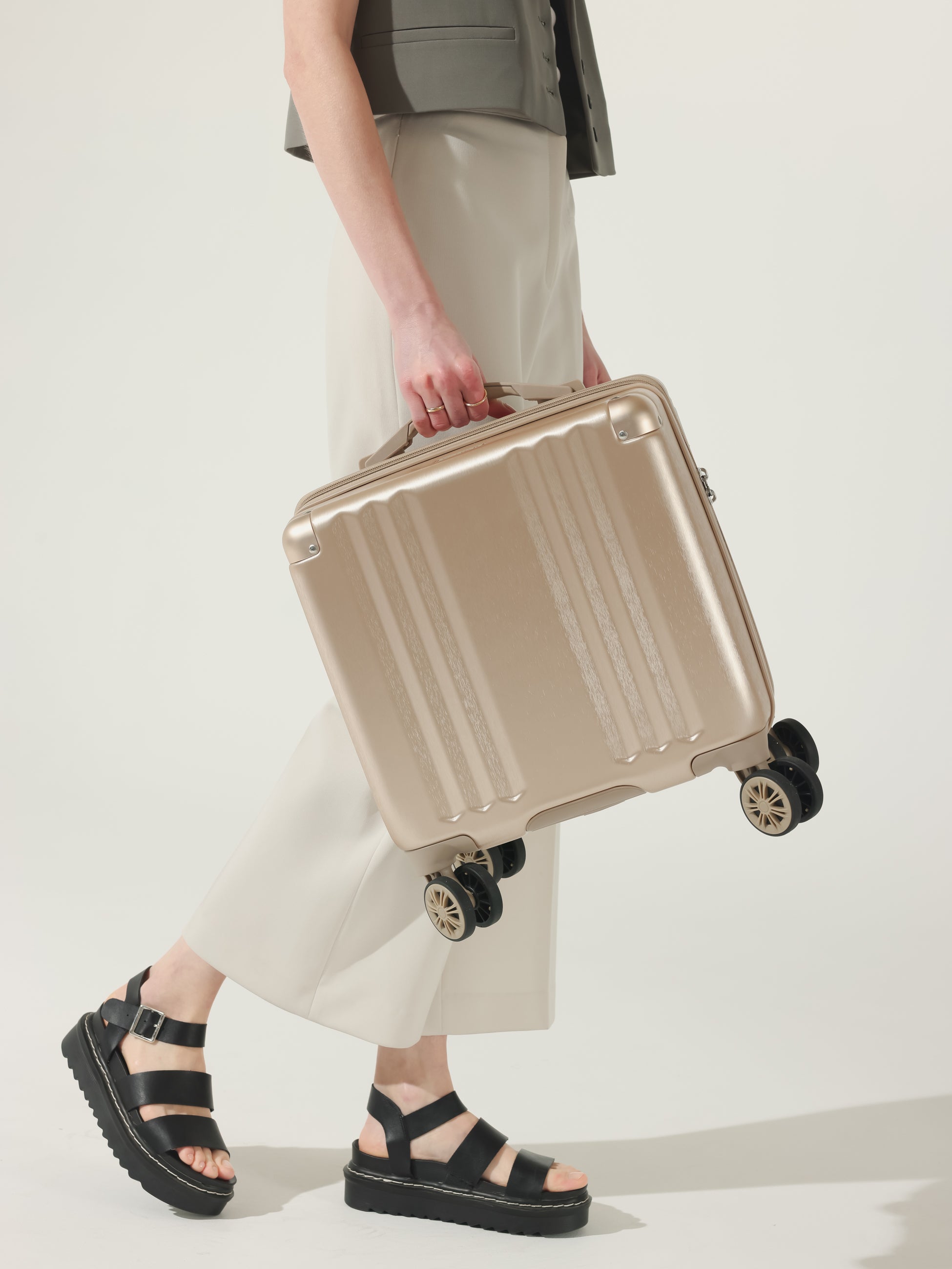 Model carrying CALPAK Ambuer 16 inch carry-on luggage with wheels and cushioned top and side handles in gold