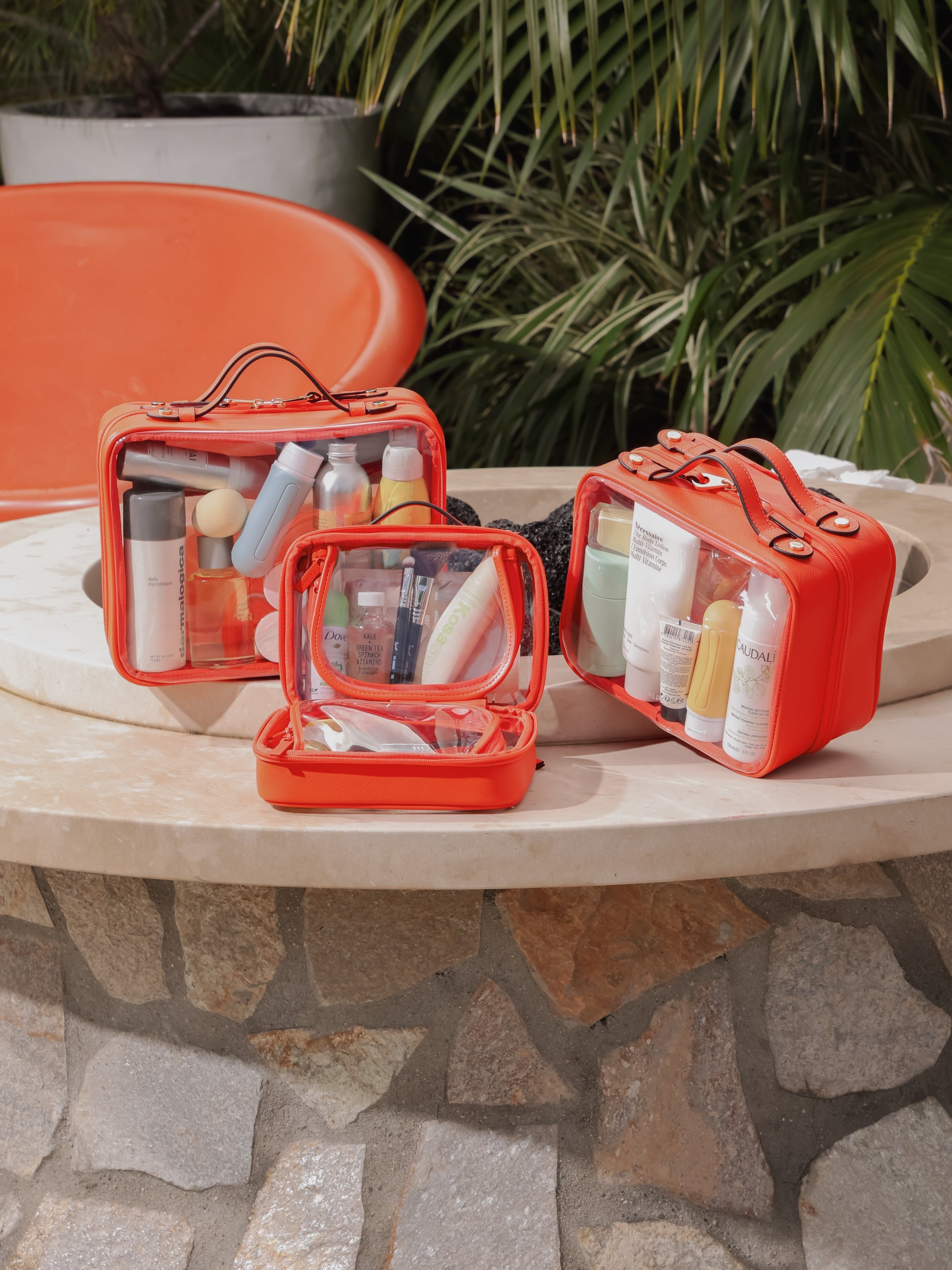 CALPAK orange clear makeup cases with zippered compartments in small, medium and large sizes