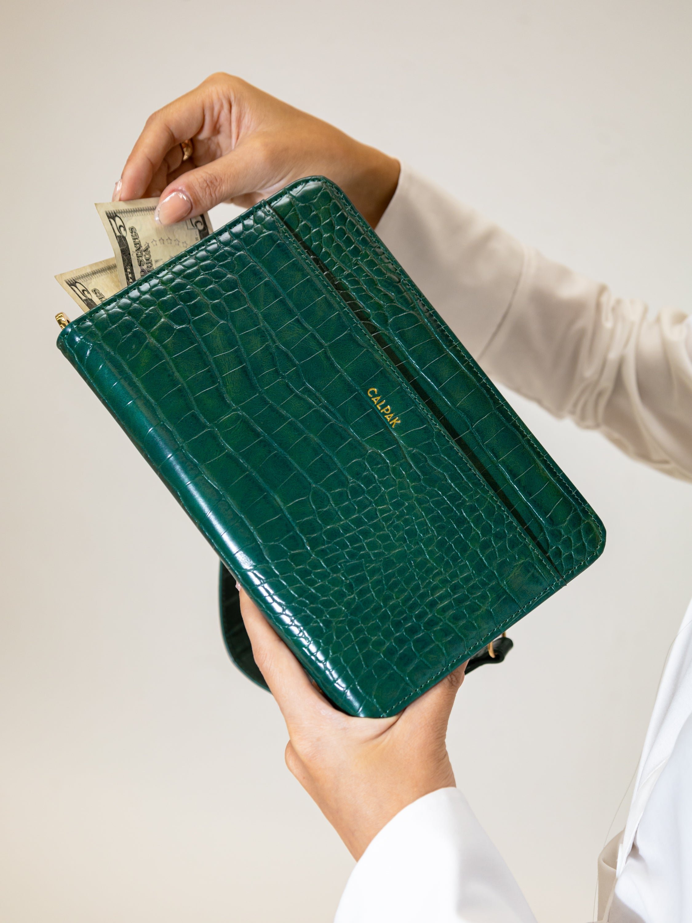 Model pulling money out of CALPAK Croc Wallet in green emerald