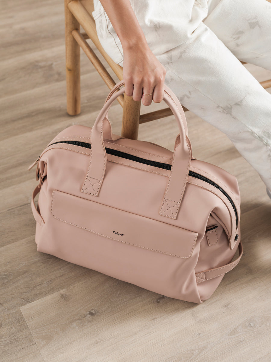 female model with faux leather pink sand CALPAK Hue duffel bag