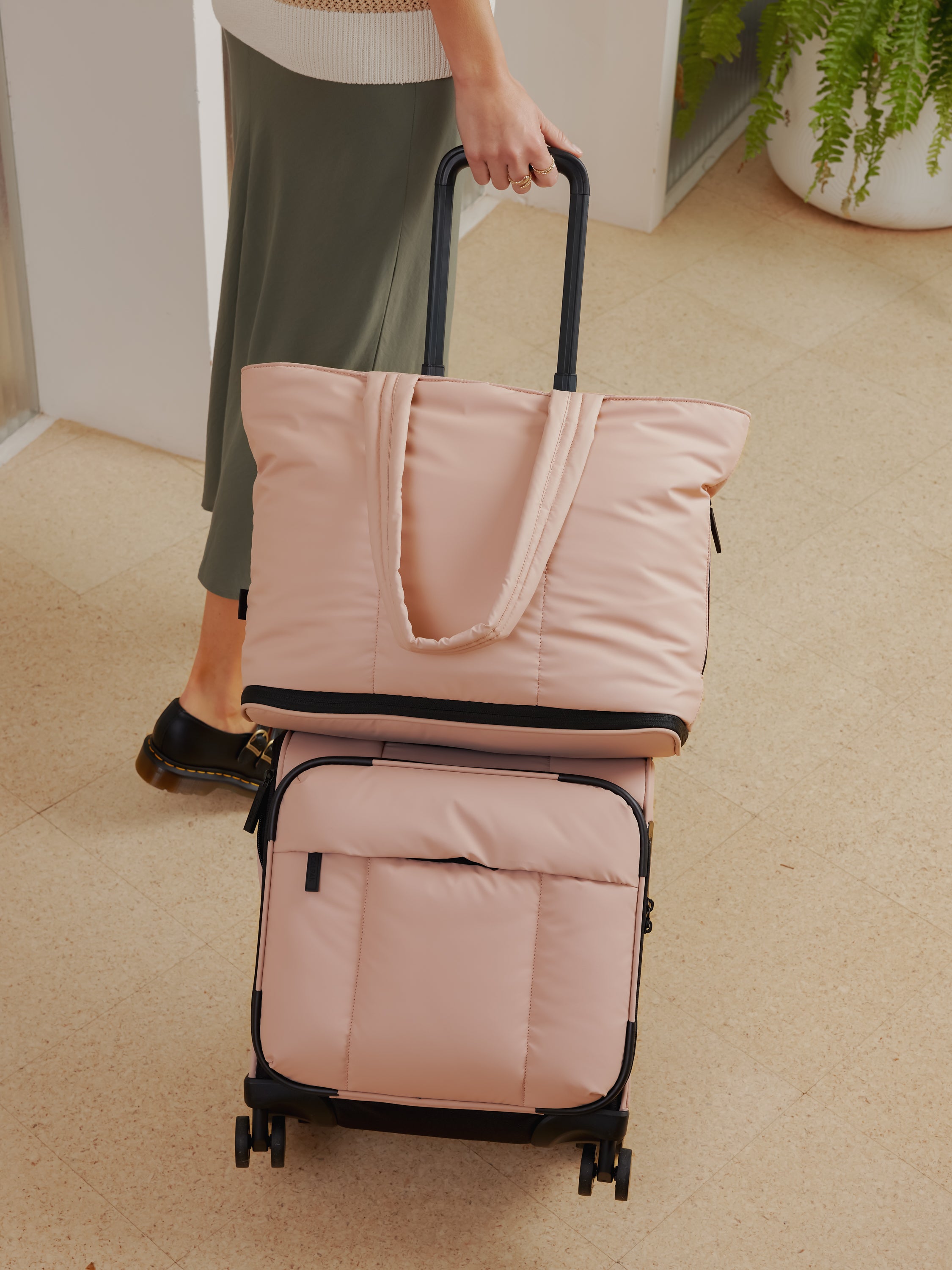 Model with CALPAK Luka expandable travel bag attached to mini carry on with trolley sleeve in rose quartz