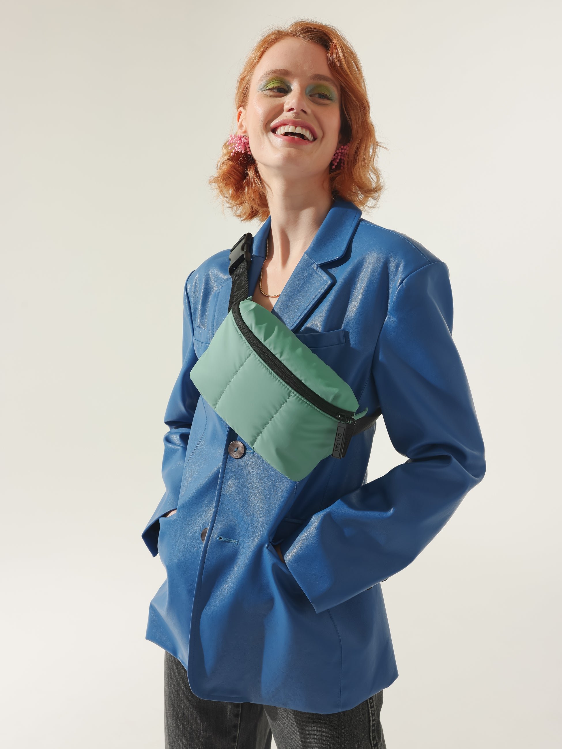 Model wearing CALPAK Luka small fanny pack as a crossbody belt bag for travel in green