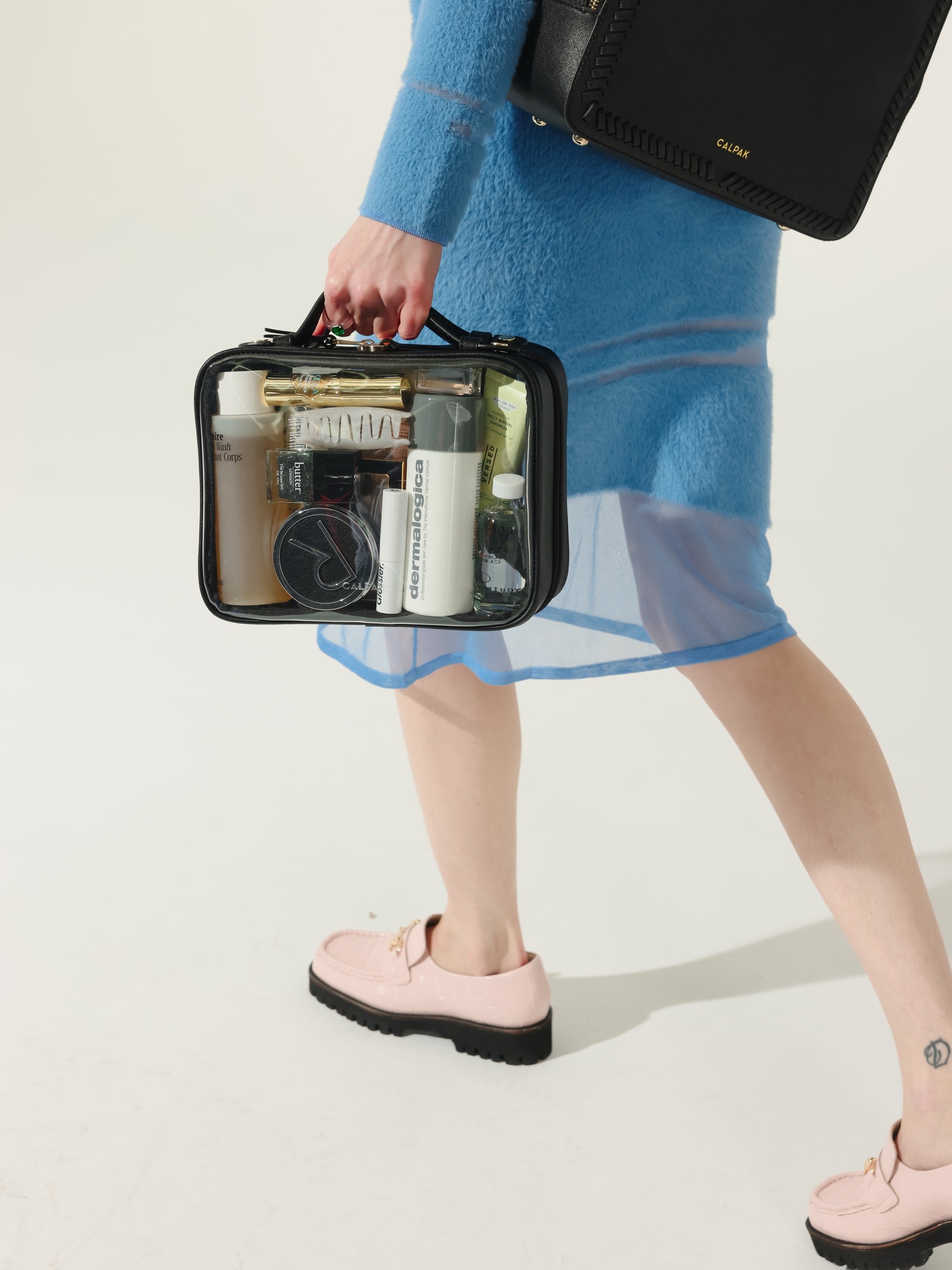 Model holding CALPAK medium transparent makeup case with top handles in black