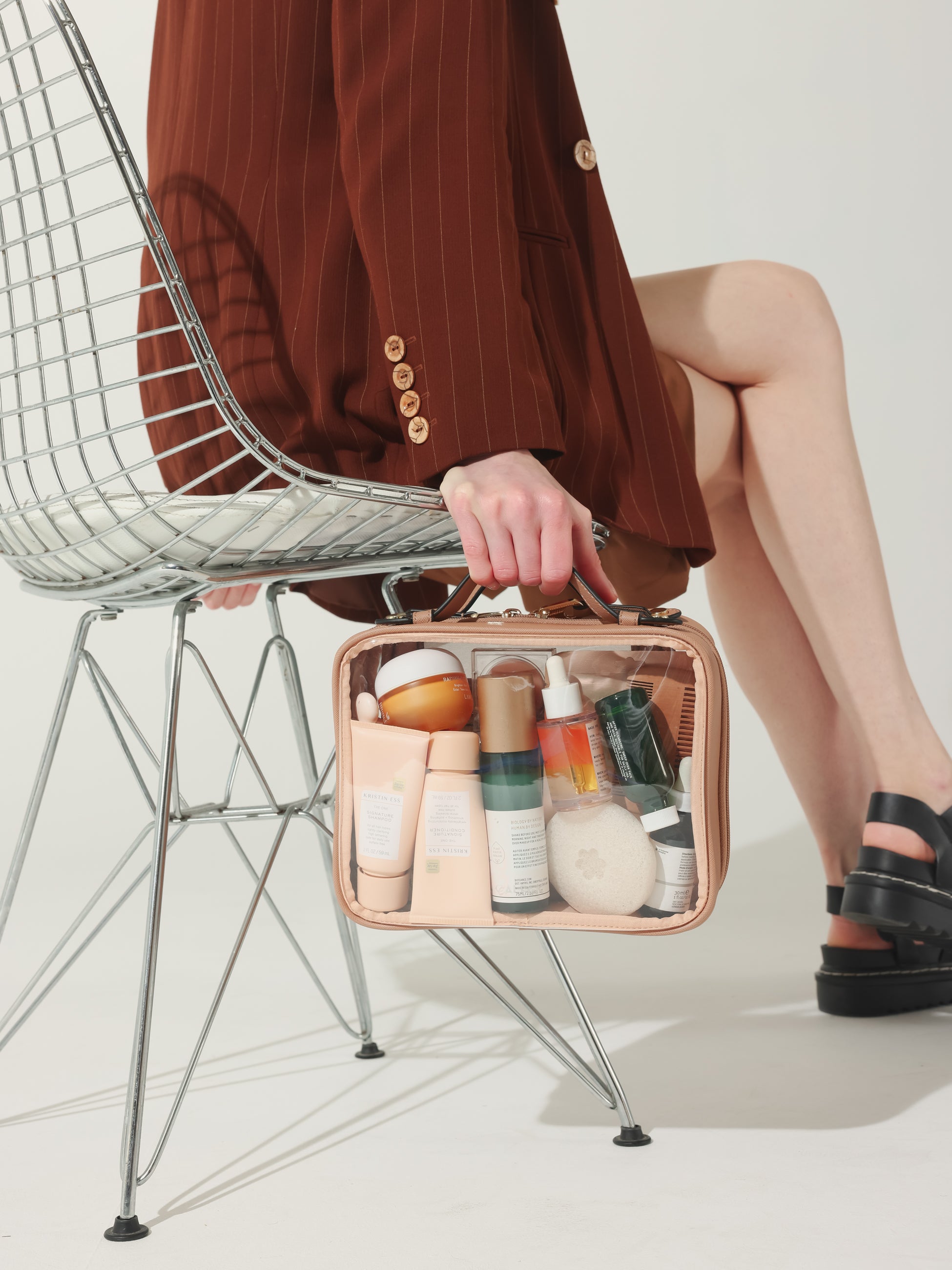 Model holding CALPAK medium clear makeup travel bag in caramel
