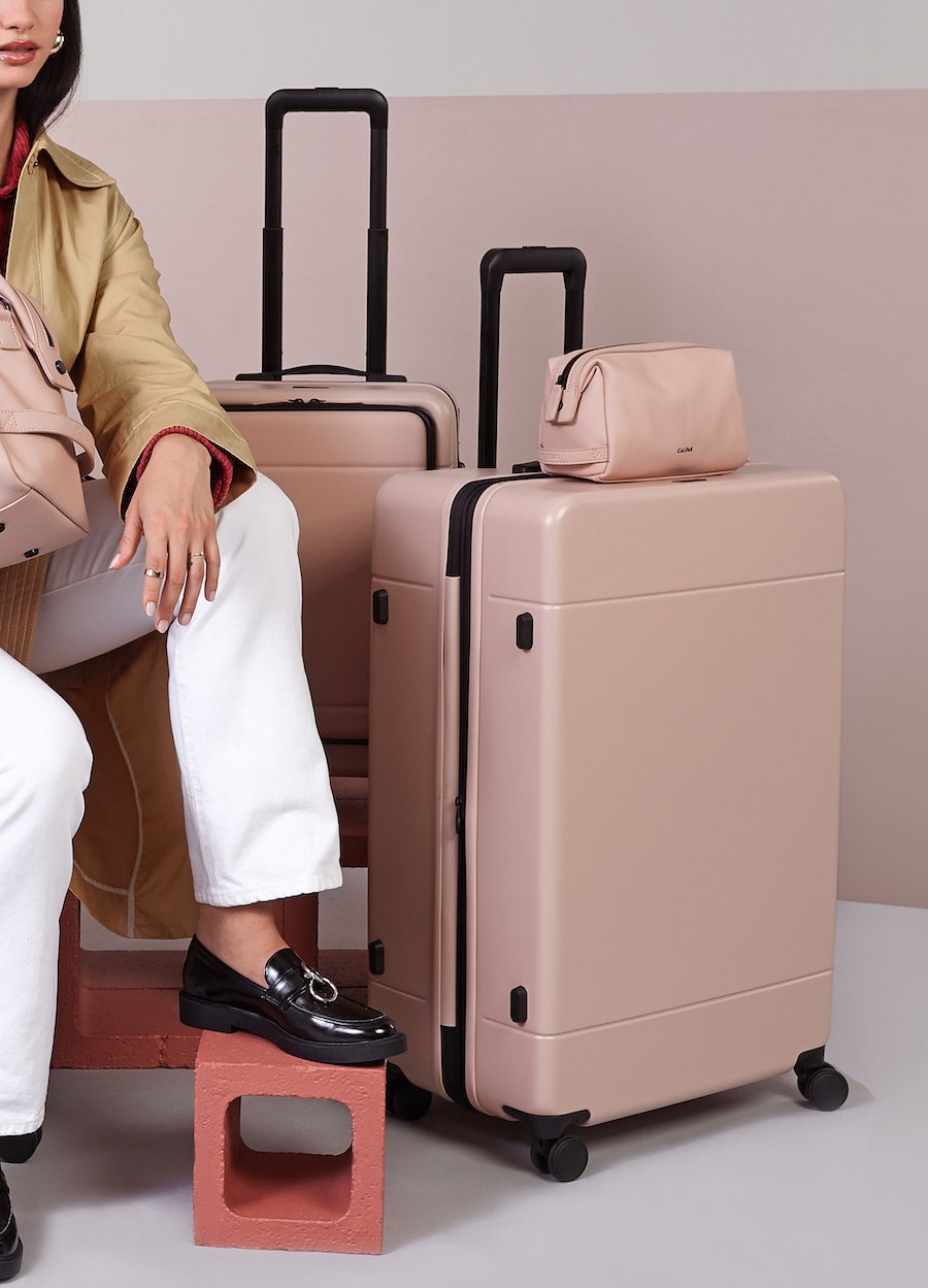 woman with large hardside polycarbonate suitcase in pink sand color from CALPAK Hue luggage collection