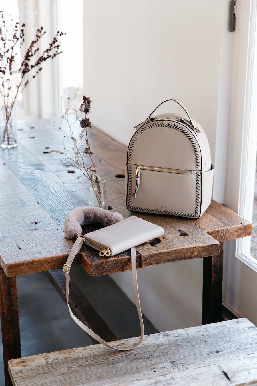 Beige CALPAK Kaya backpack with travel wallet on the table
