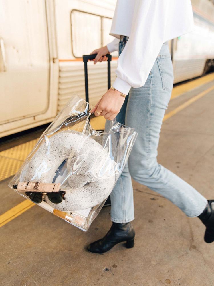 model carries clear bag with white silk travel neck pillow and sleeping mask